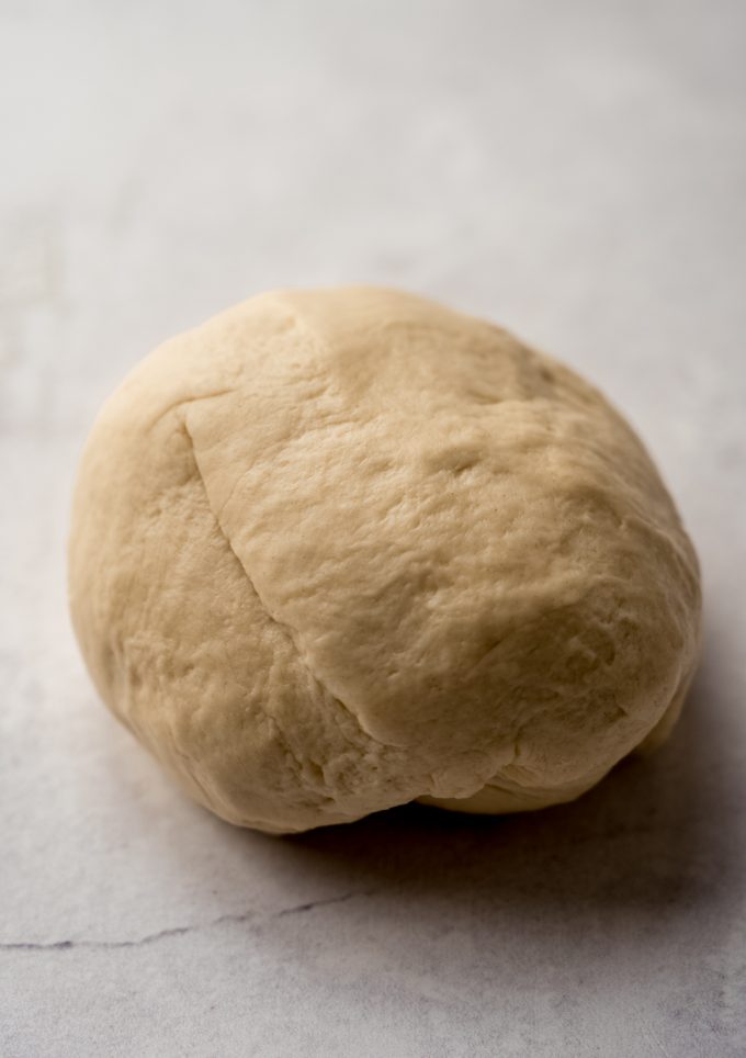 A ball of yeasted cinnamon roll dough on a surface.