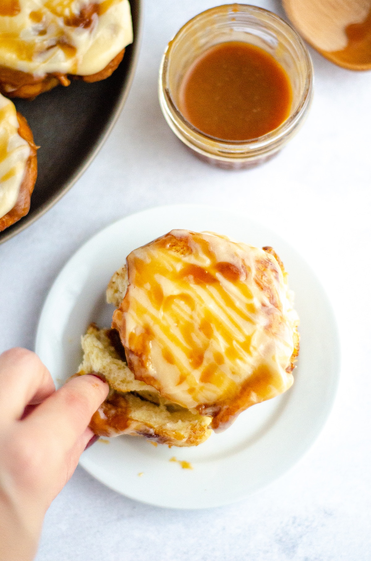 fingers pulling apart caramel rolls with caramel cream cheese frosting
