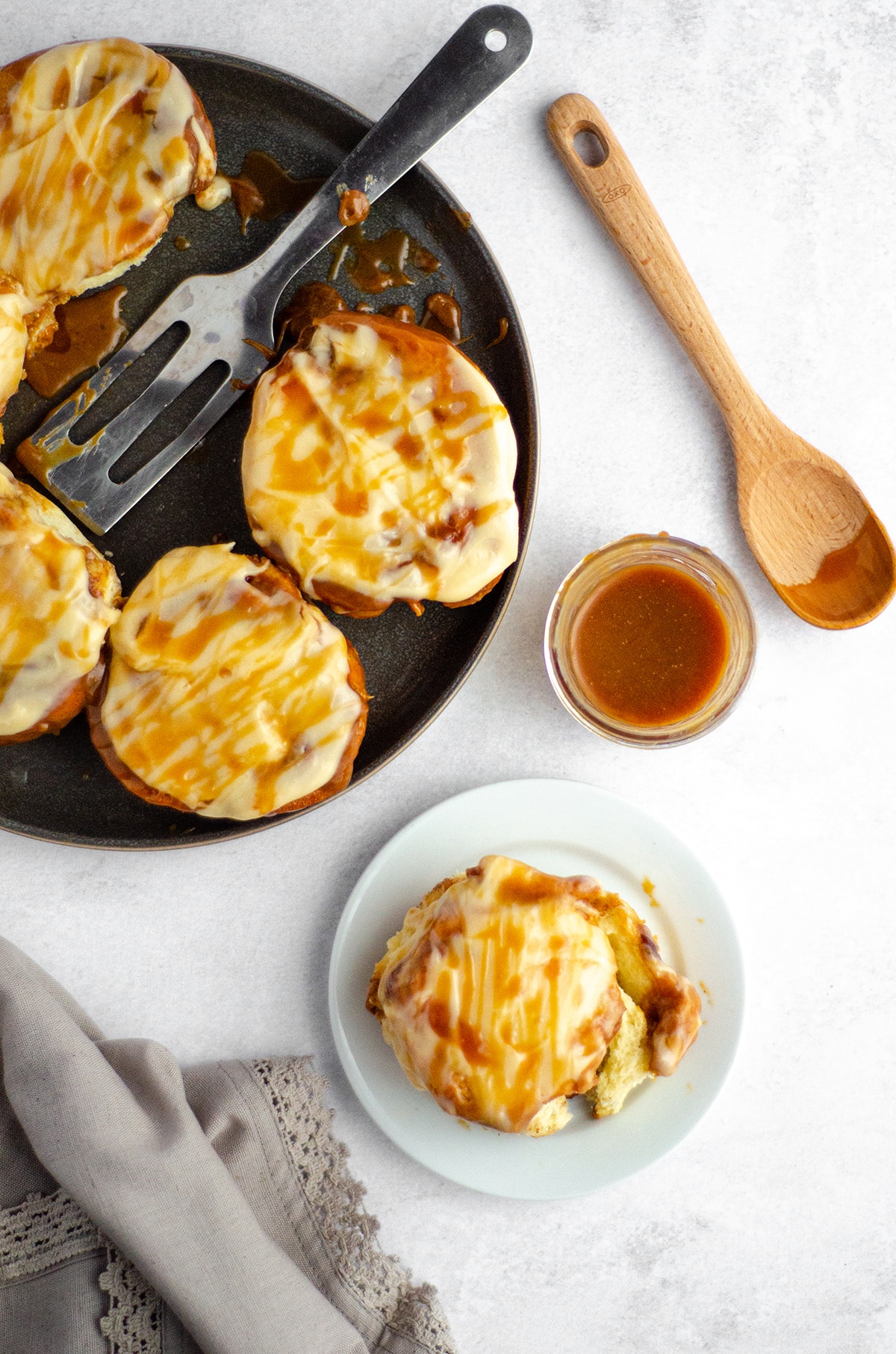 aerial photo of caramel roll on a white plate with a plate of caramel rolls and a jar of caramel sauce off to the side