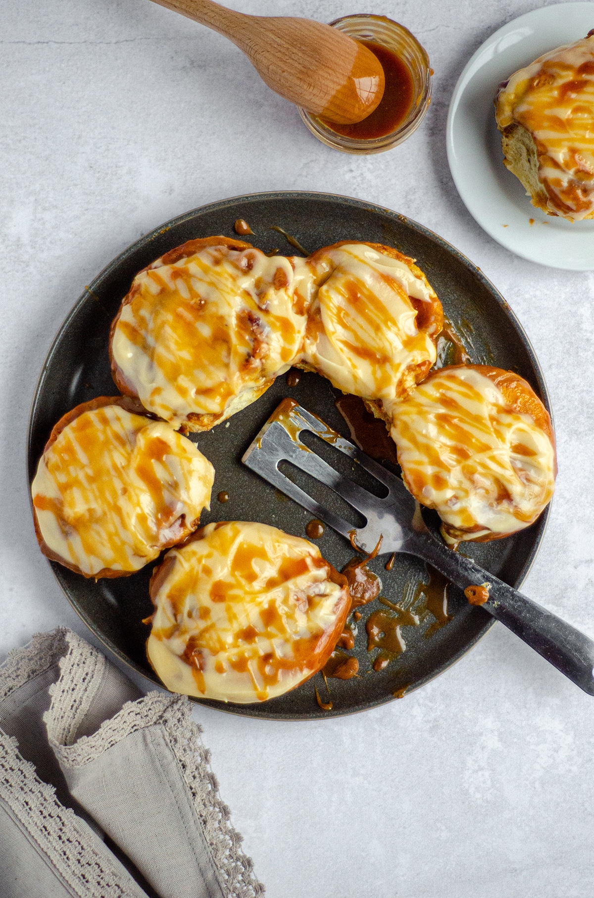 aerial photo of caramel rolls with caramel cream cheese frosting on a plate with a serving spatula