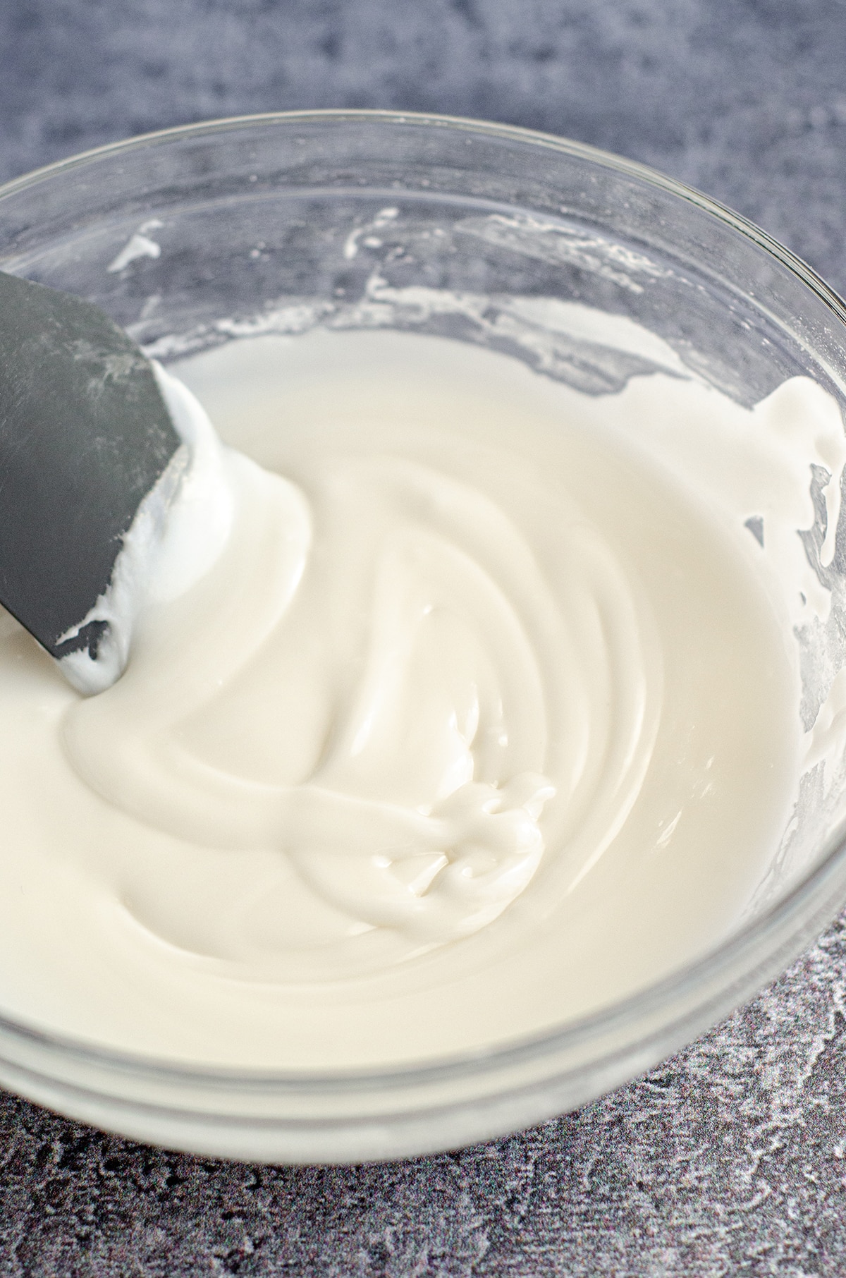 bowl of royal icing with a gray spatula sitting in it, testing to see if the drizzle is disspiating