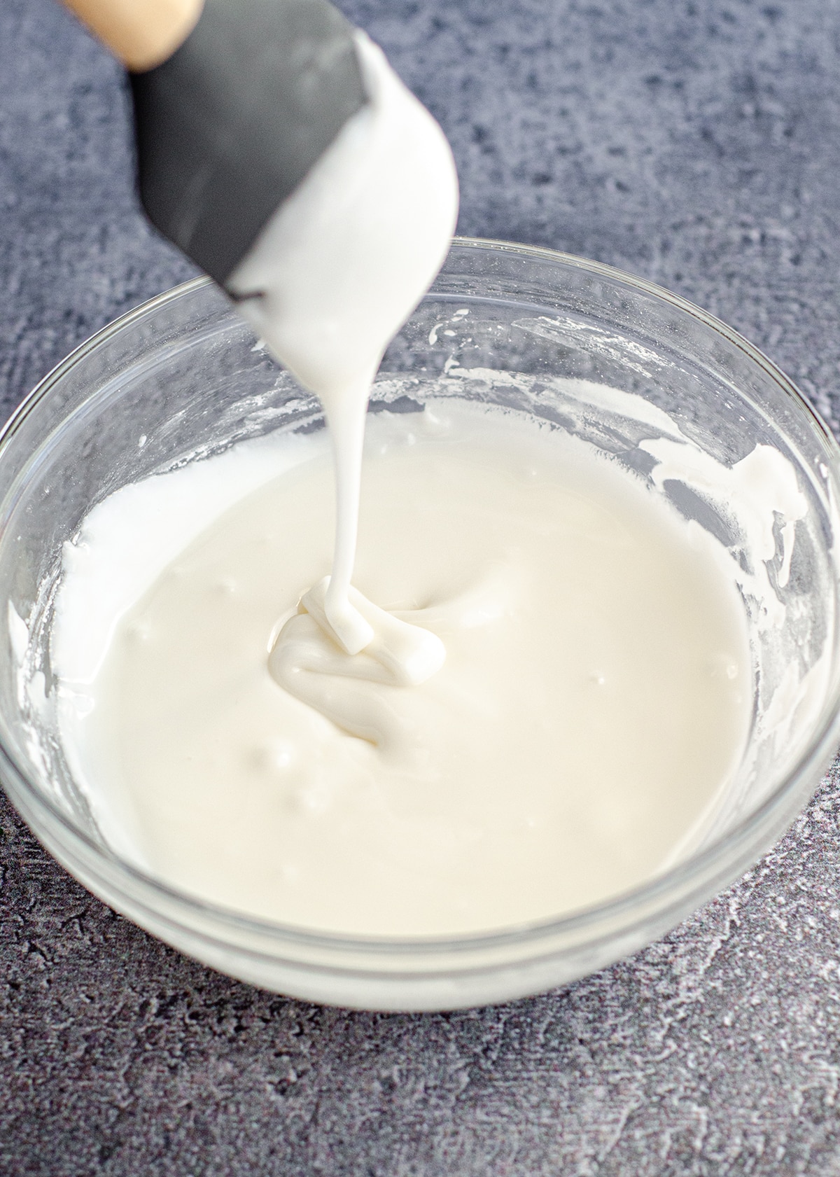 spatula dripping easy royal icing into a glass bowl