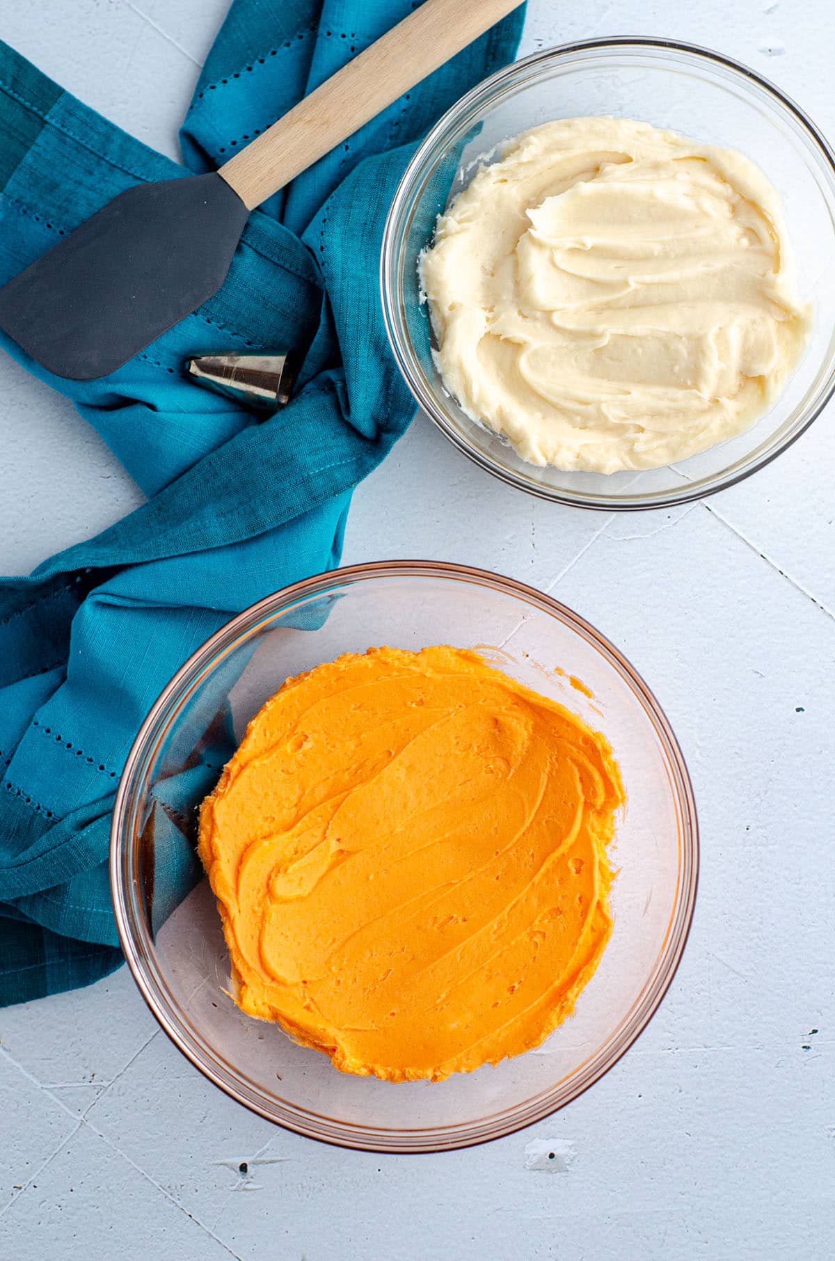 aerial photo of two bowls of frosting (one white and one orange) to swirl together for orange creamsicle frosting