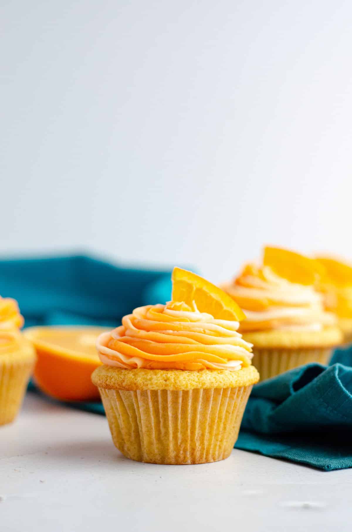 orange creamsicle cupcake in front of a turquoise kitchen towel and orange slices