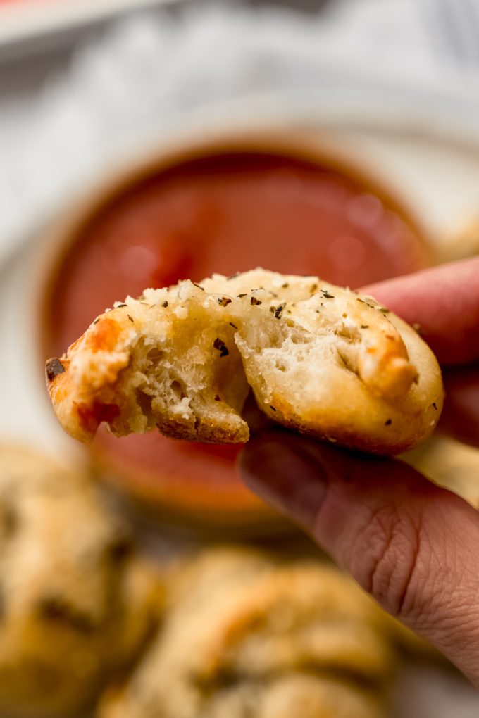 Someone is holding a homemade garlic knot with a bite taken out of it.