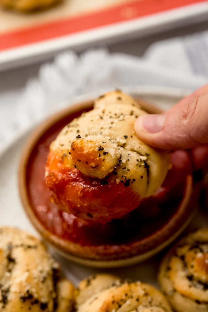 Someone is dipping a homemade garlic knot into marinara sauce.