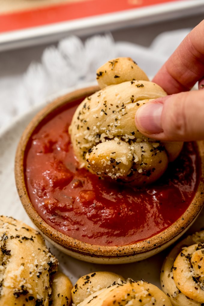 Someone is dipping a homemade garlic knot into marinara sauce.