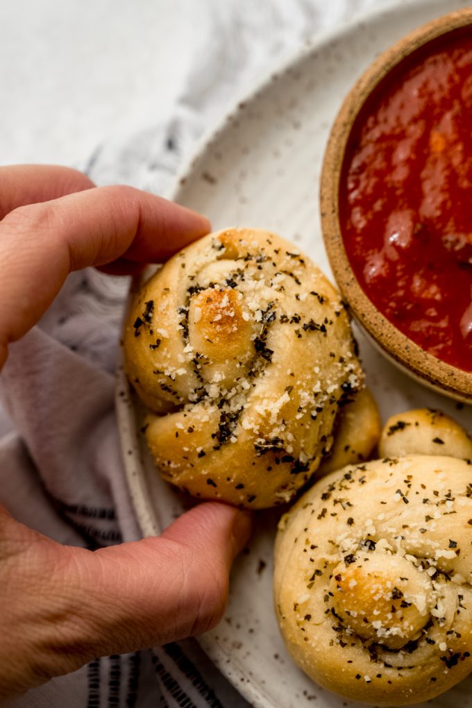 Someone is grabbing a garlic knot from a plate.