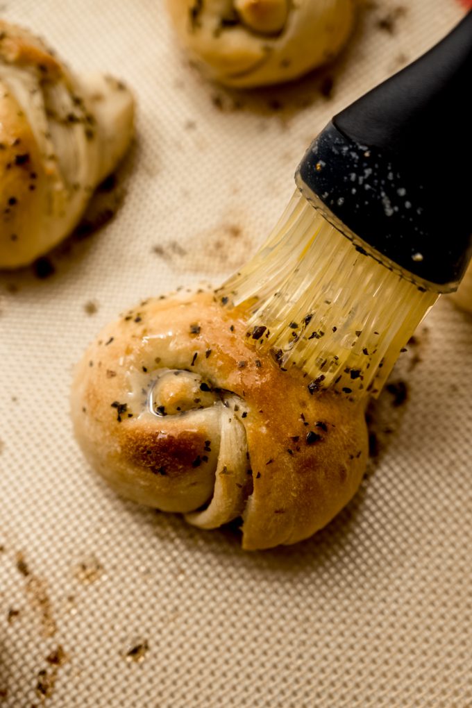 Someone is brushing a garlic knot with herbed garlic butter.