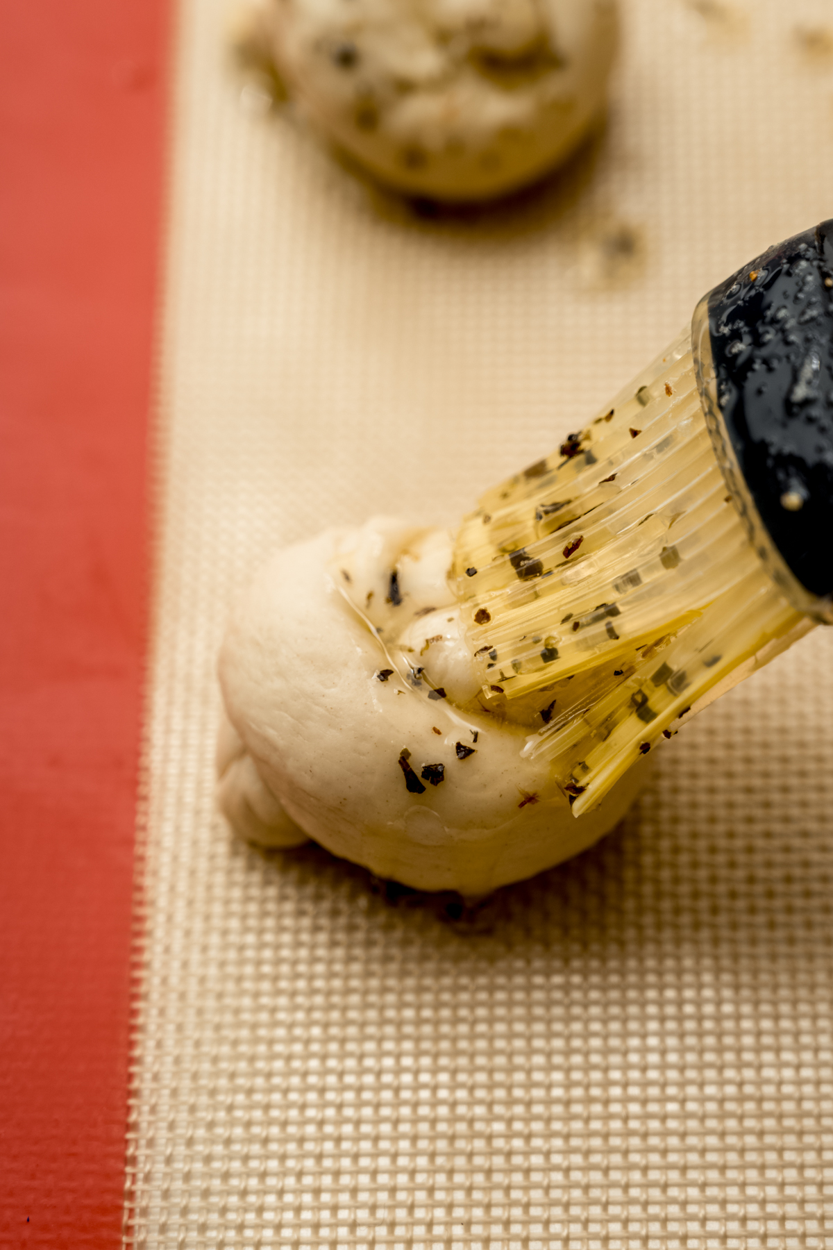 Someone is brushing a garlic knot with herbed garlic butter.