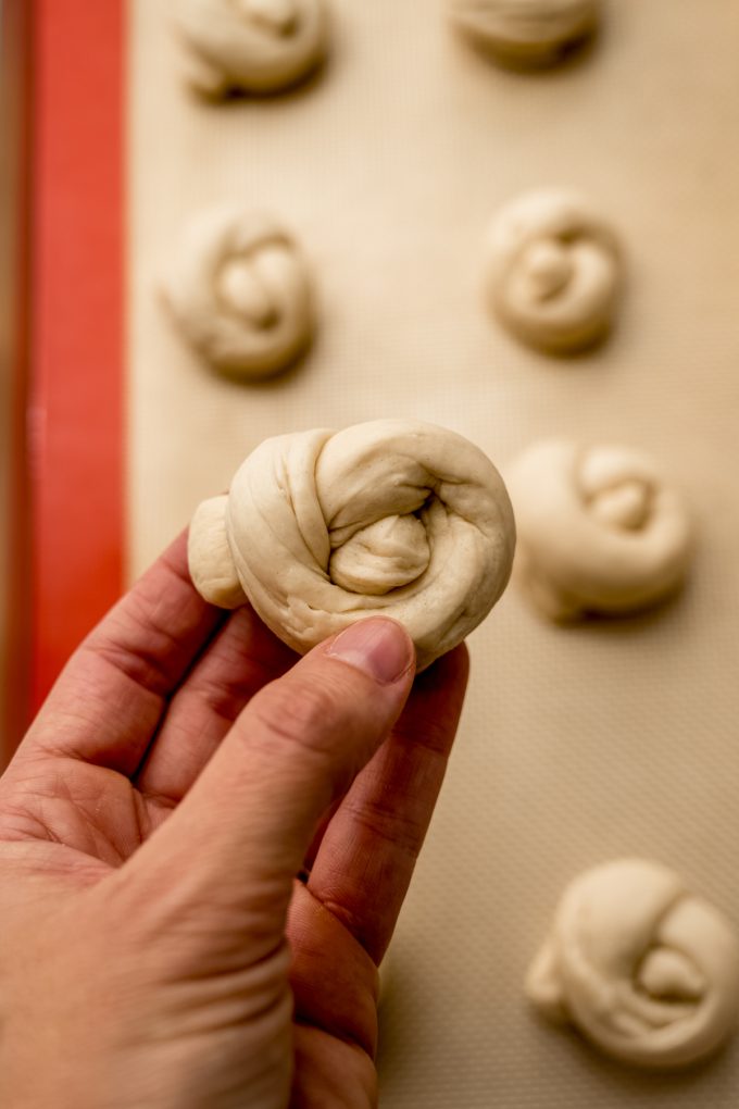 Someone's hand holding a piece of dough that they're forming into a garlic knot.