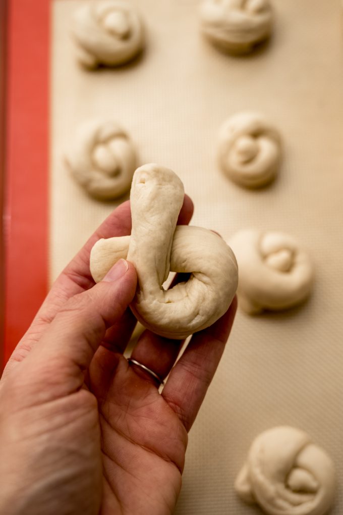 Someone's hand holding a piece of dough that they're forming into a garlic knot.
