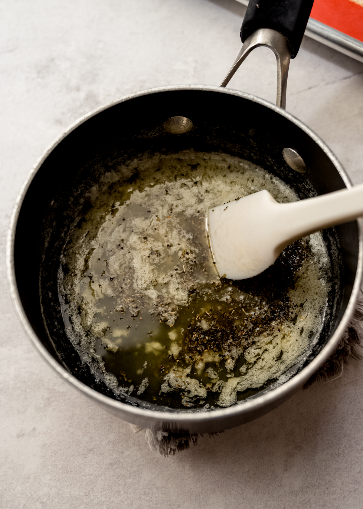 A saucepan of herbed garlic butter with a spatula in it.