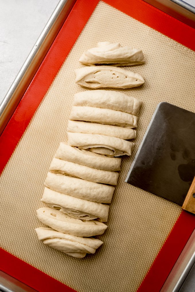 Someone is using a bench scraper to portion dough into equal pieces to make homemade garlc knots.