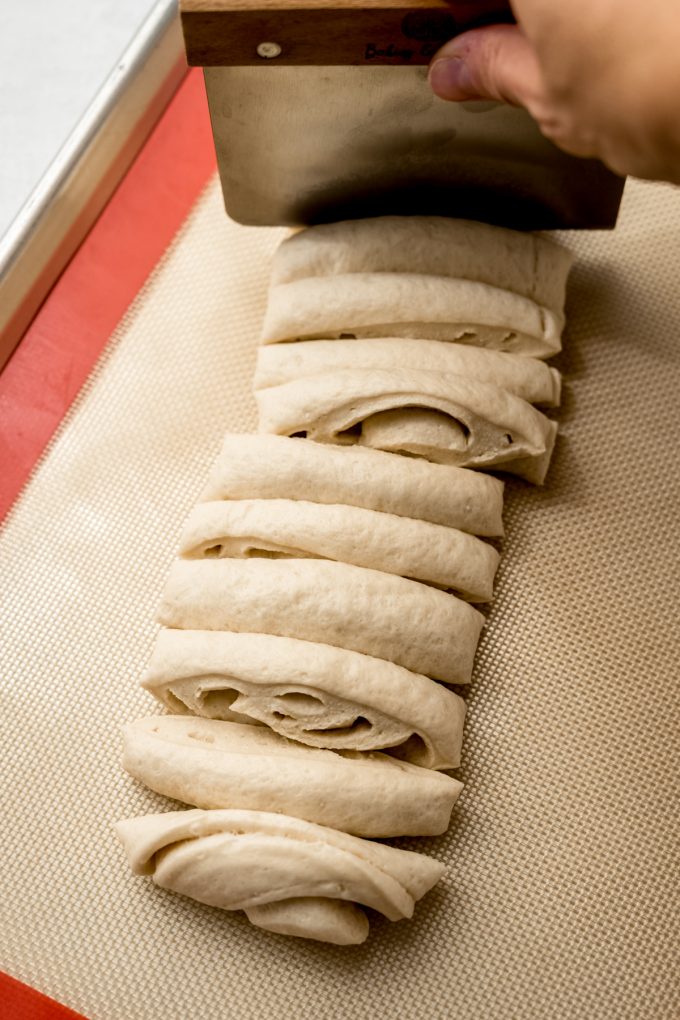 Someone is using a bench scraper to portion dough into equal pieces to make homemade garlc knots.