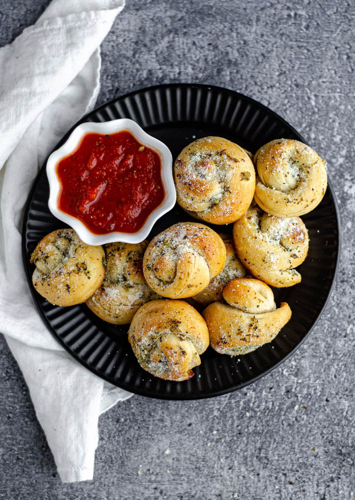 aerial photo of homemade garlic knots on a black plate with a cup of marinara