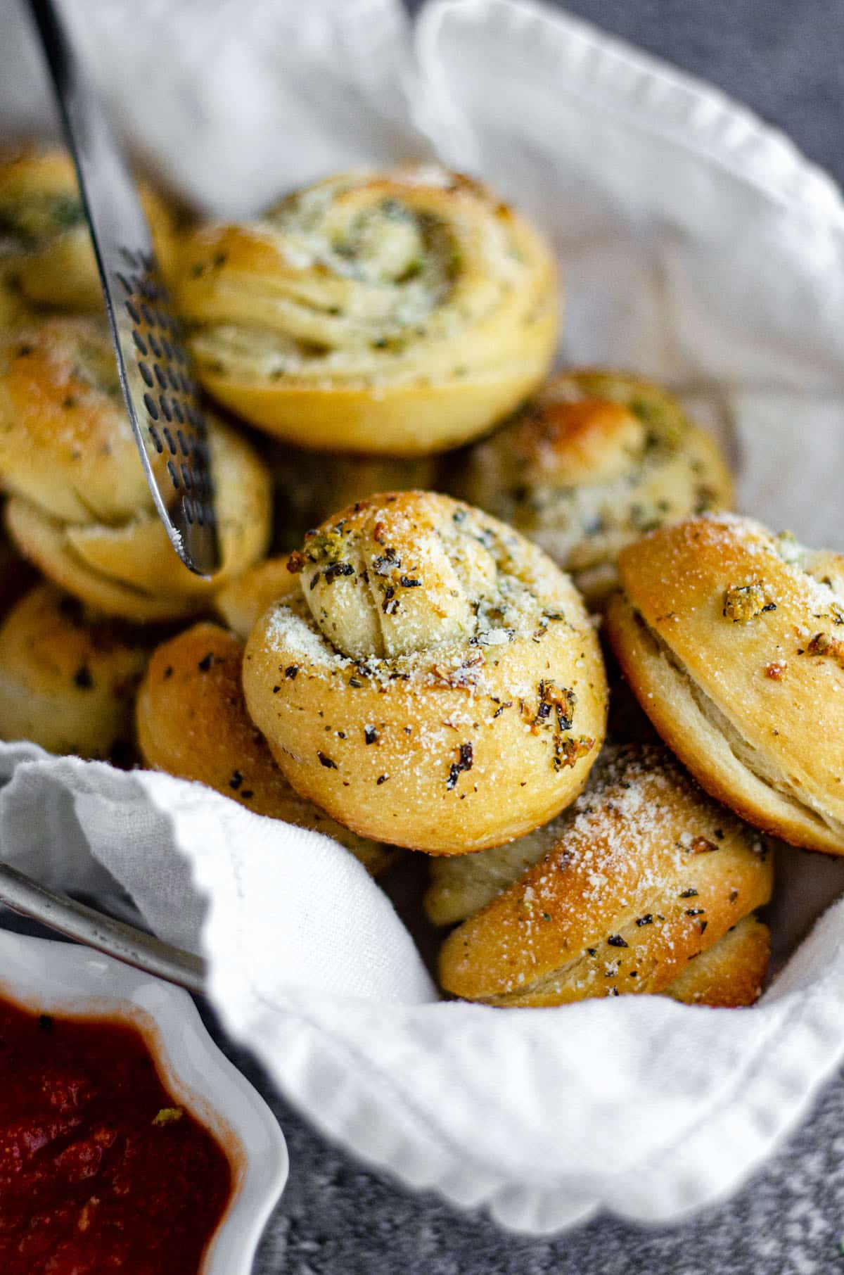 homemade garlic knots in a basket with metal tongs