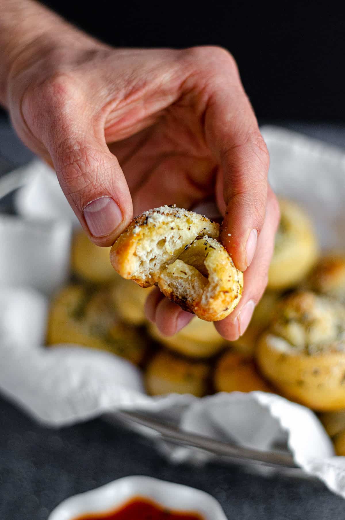 hand holding a homemade garlic knot with a bite taken out of it