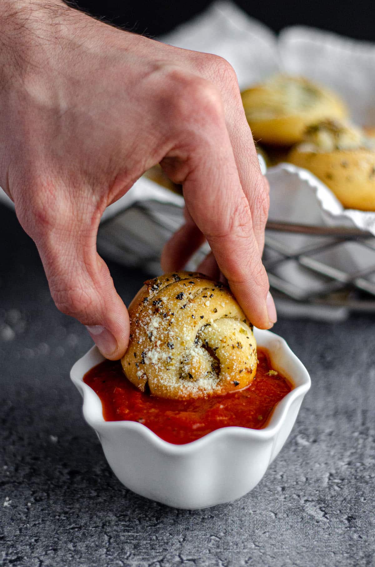 hand dipping a homemade garlic knot into marinara