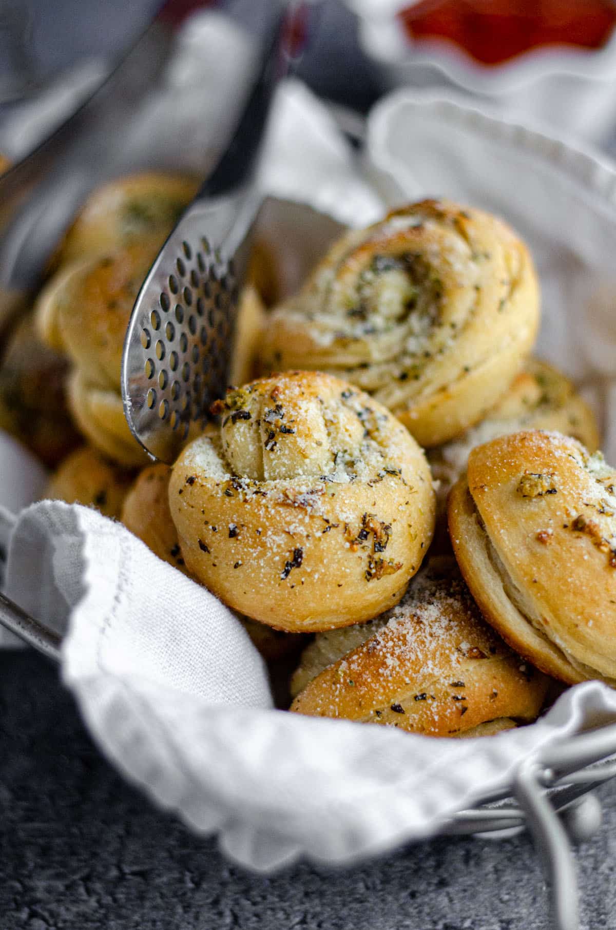 homemade garlic knots in a basket with metal tongs