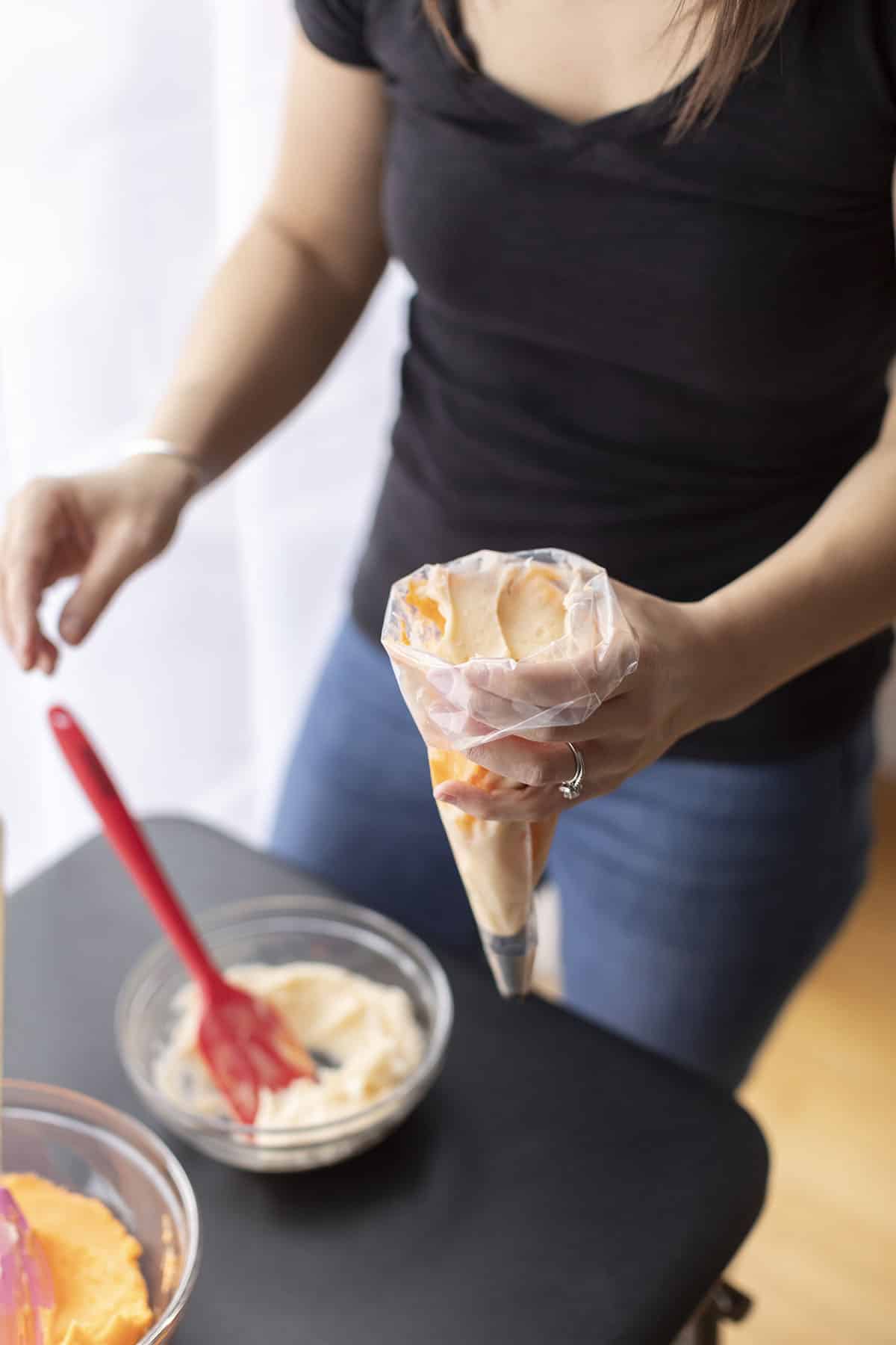 woman holding a piping bag and filling it with orange creamsicle frosting