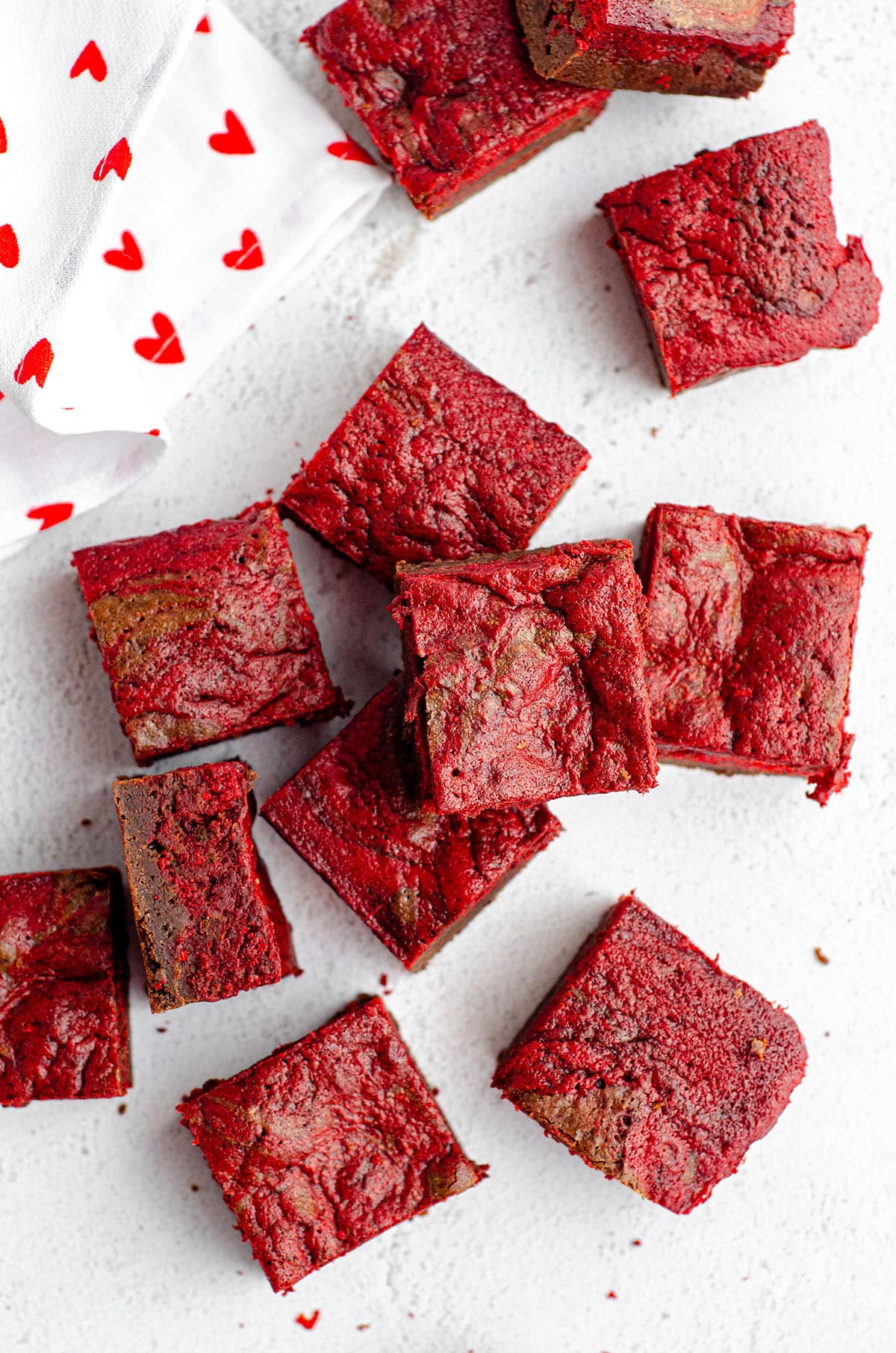 red velvet brownies cut into squares and scattered around with a white kitchen towel with red hearts on it