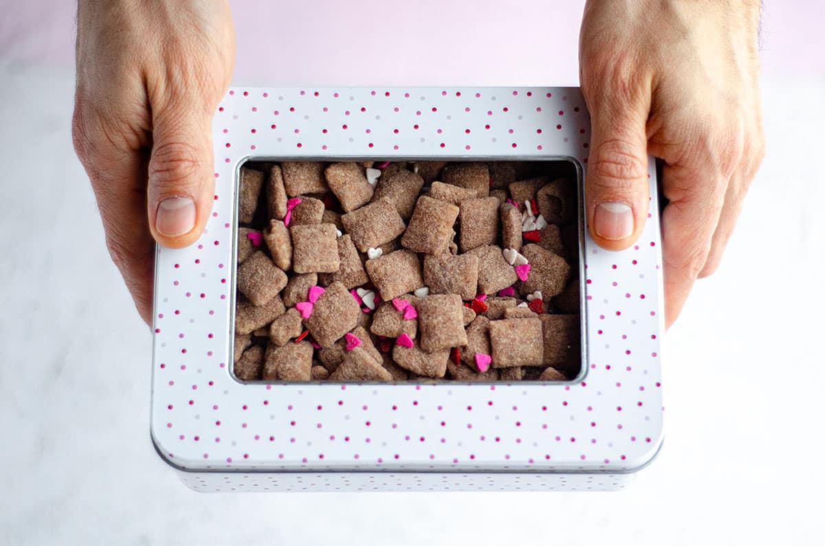 hands holding a treat box filled with red velvet puppy chow