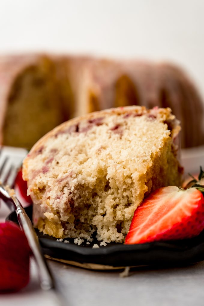 A slice of strawberry Bundt cake on a plate with a fork and a bite has been taken out of the cake.