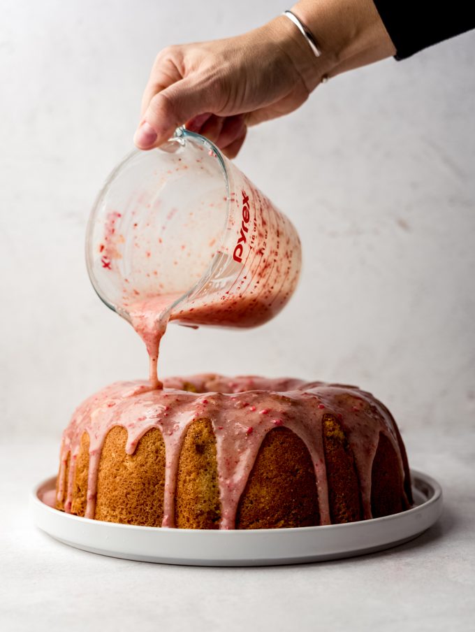 Someone is pouring strawberry ganache onto a strawberry Bundt cake.