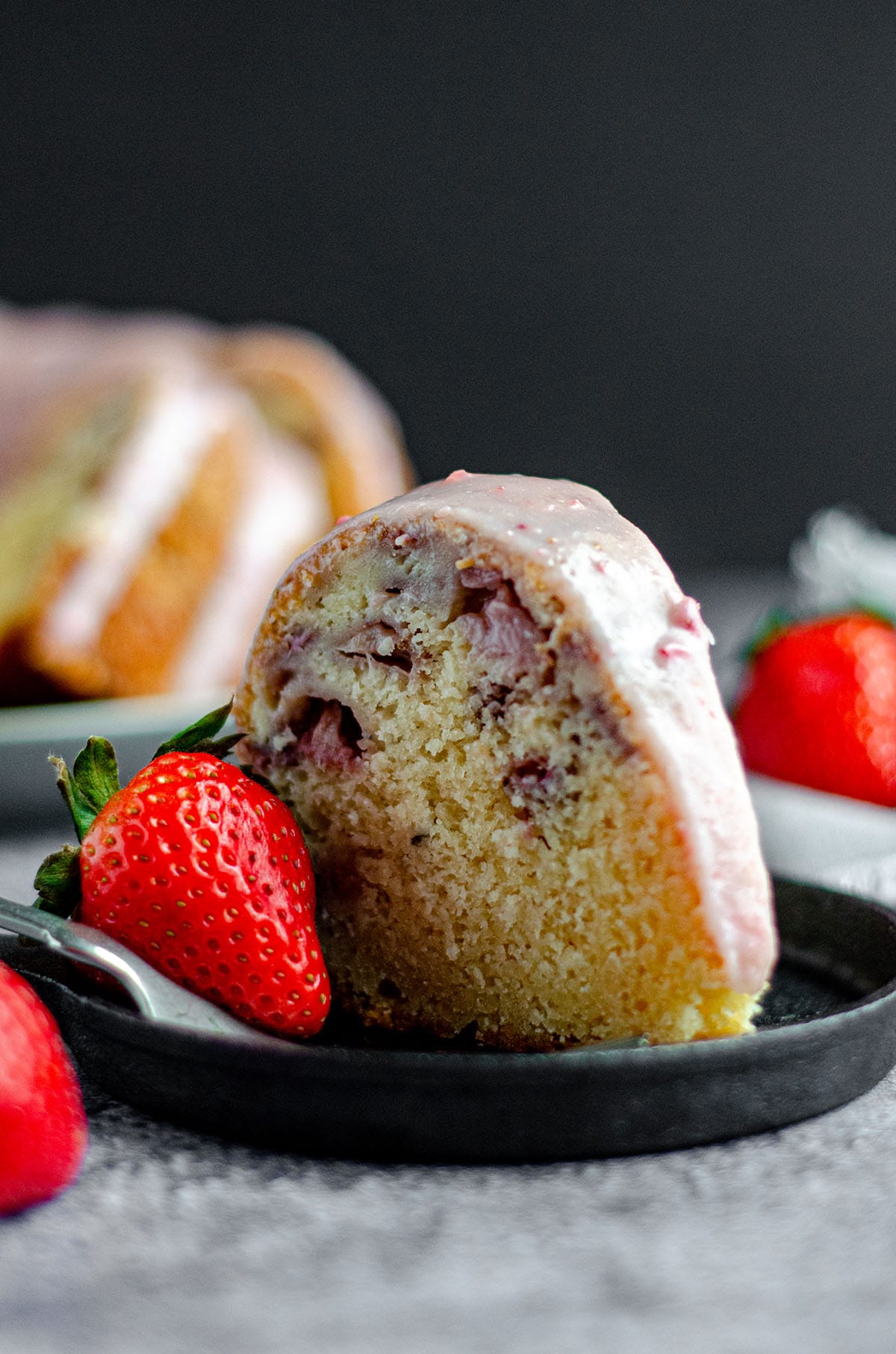 slice of a strawberry bundt cake on a plate with a strawberry as garnish