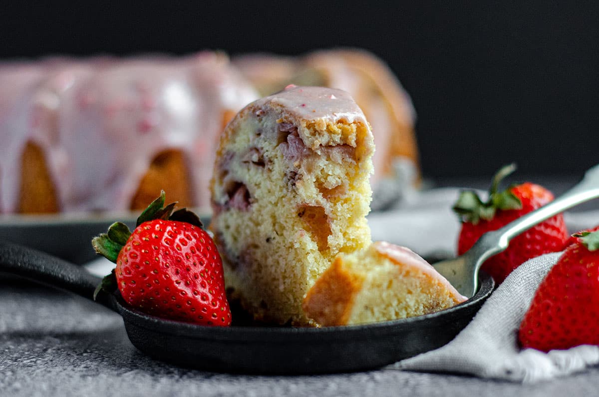 strawberry bundt cake sitting on a plate with a forkful taken out of it