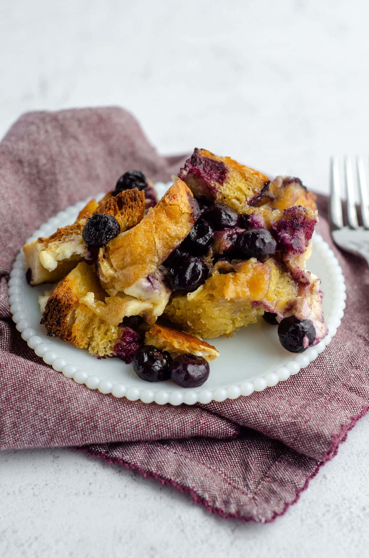 baked blueberry french toast sitting on a white plate with a plum colored kitchen towel