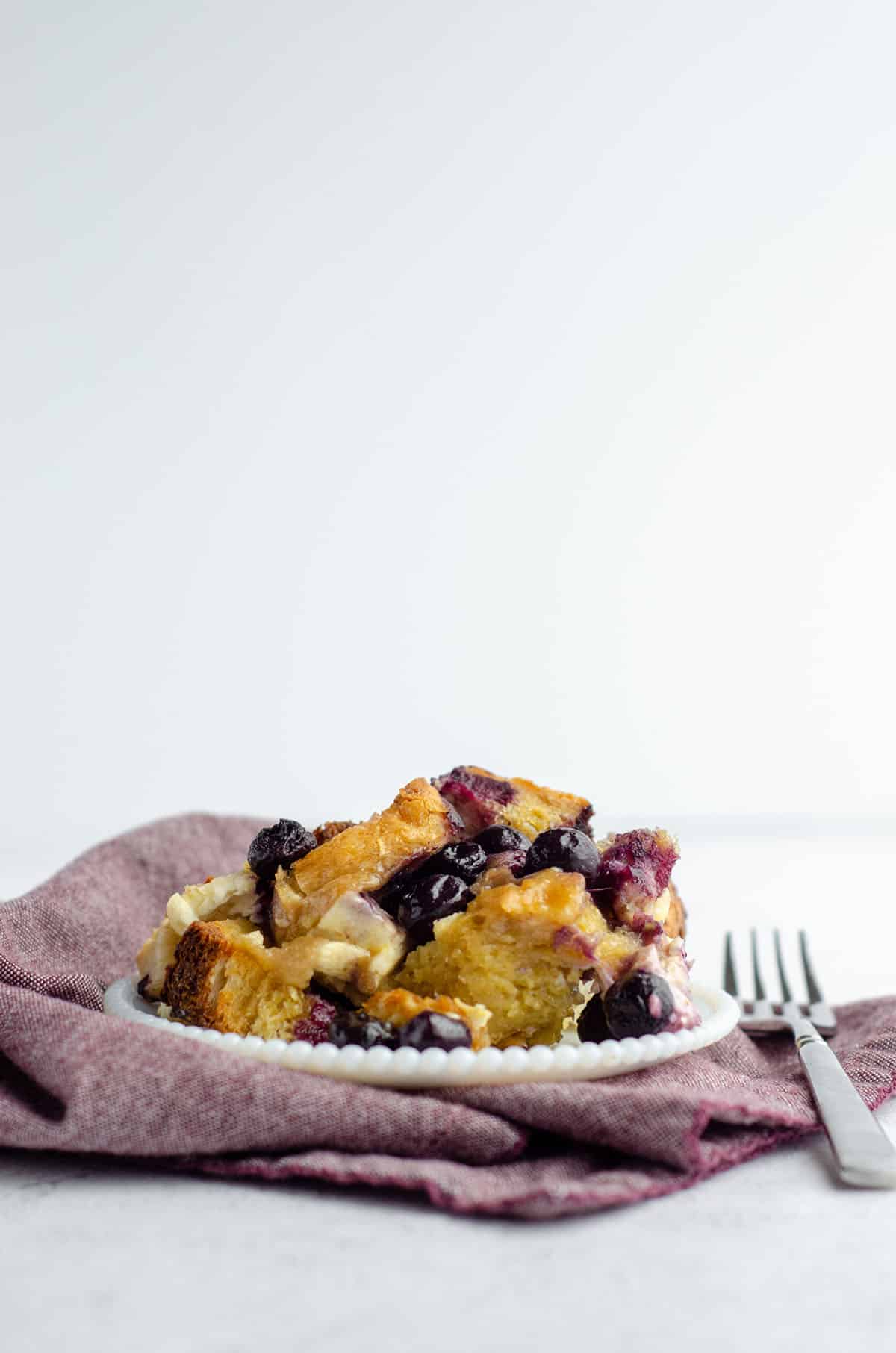 baked blueberry french toast on a white plate sitting on a plum colored kitchen towel