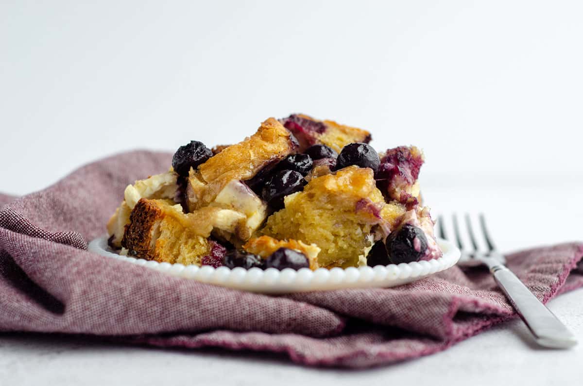 baked blueberry french toast on a white plate sitting on a plum colored kitchen towel
