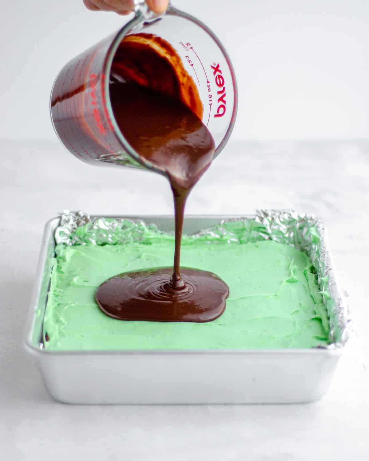 pouring chocolate onto mint layer of mint chocolate brownies 