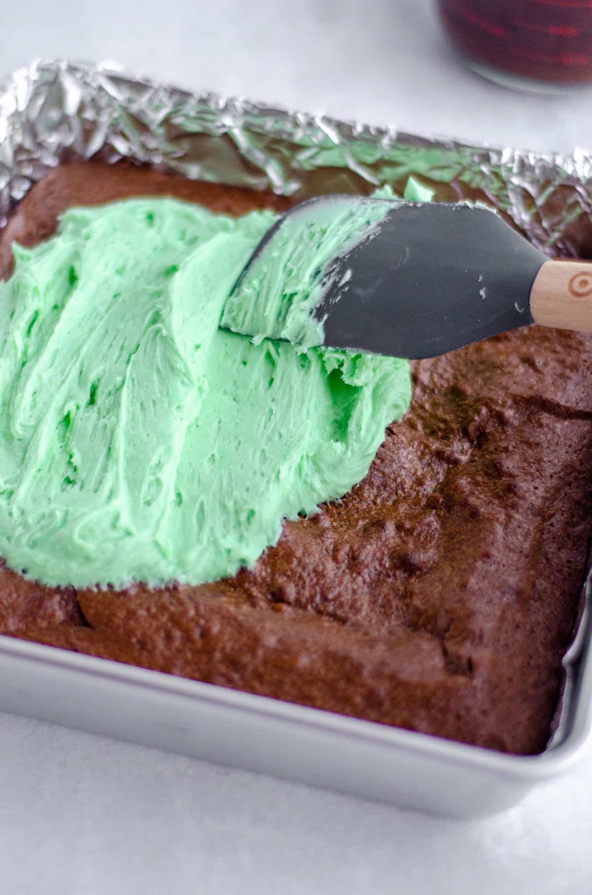 spatula spreading green mint buttercream onto brownies 