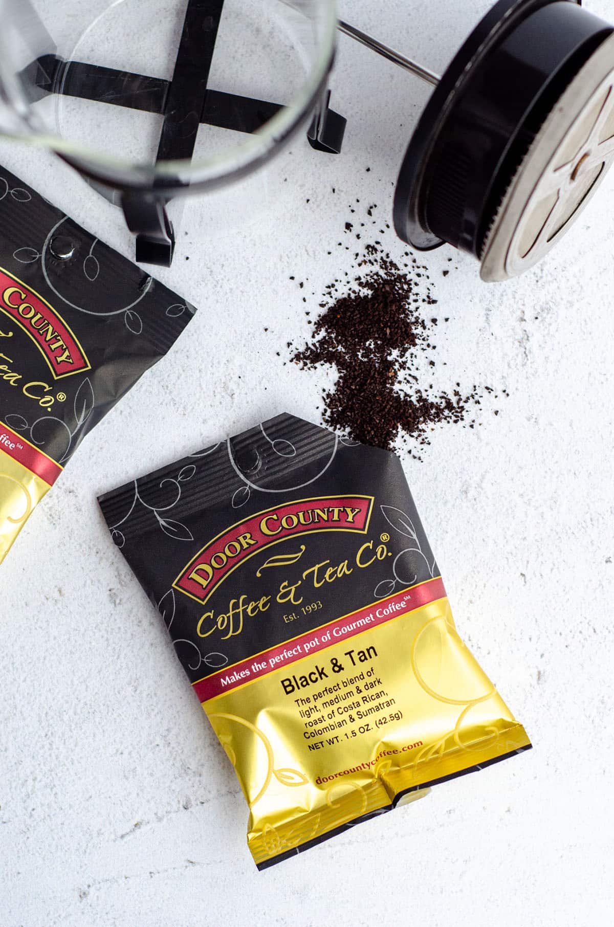 coffee grounds poured out of a tipped over bag of coffee beans and a french press in the background