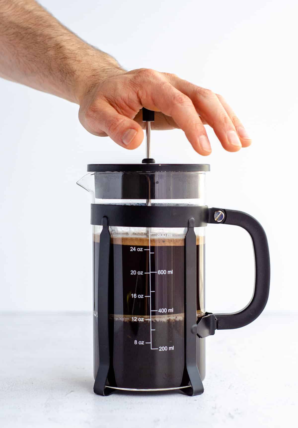 a hand pressing down the plunger on a french press coffee maker