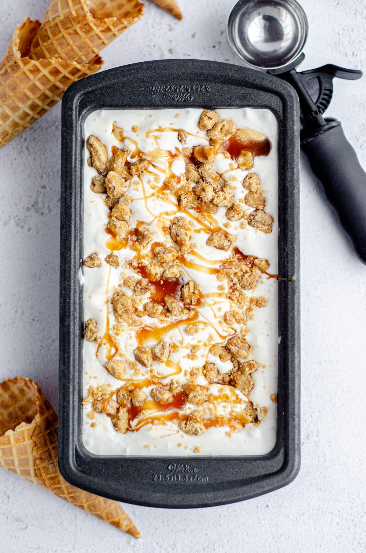 aerial photo of homemade praline ice cream in a loaf pan with ice cream cones and an ice cream scoop around it