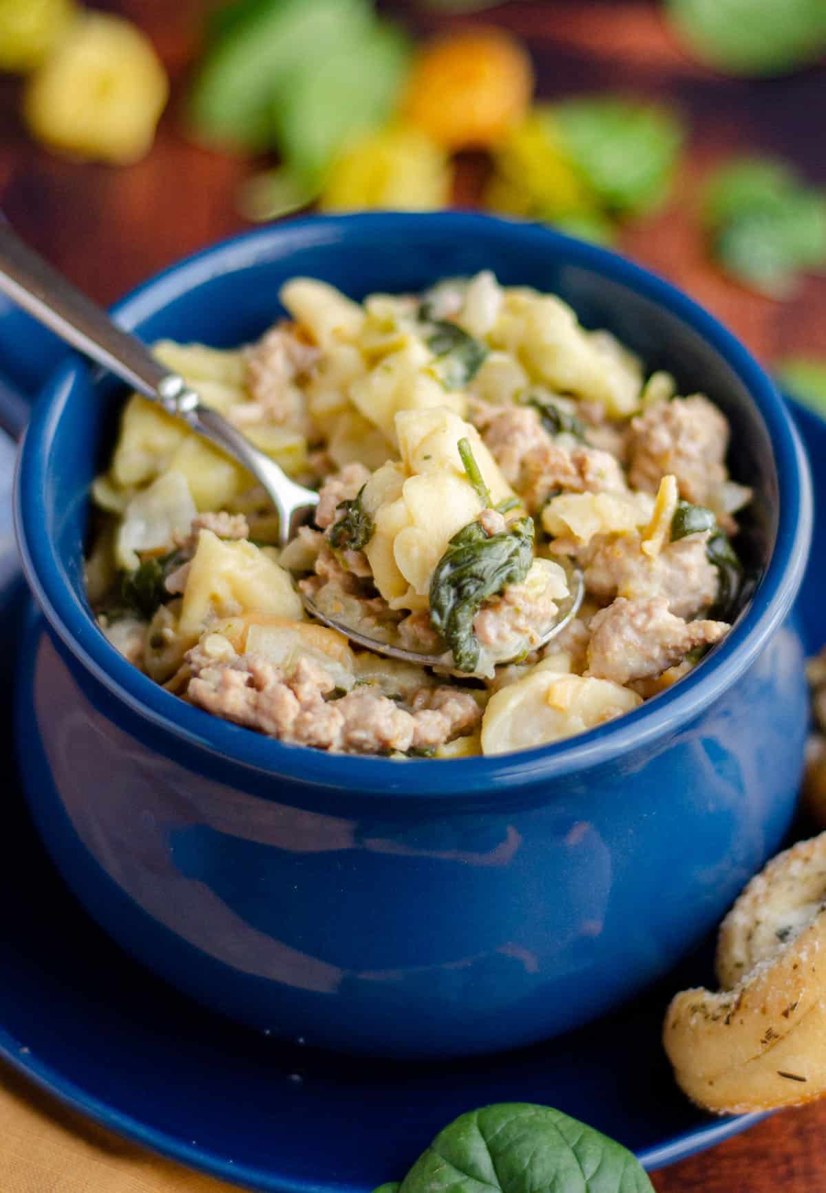 sausage tortellini soup in a blue bowl with a spoon scooping out a bite