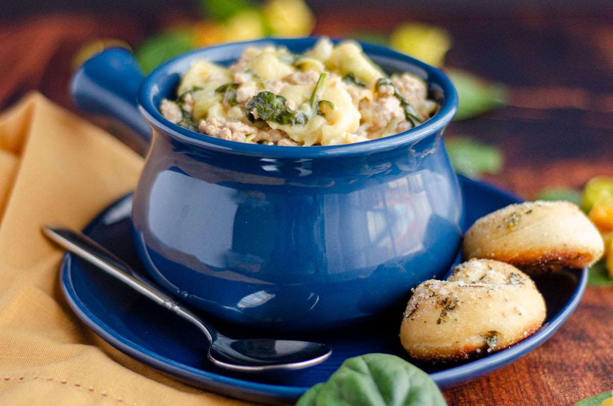 sausage tortellini soup in a blue bowl on a blue plate with garlic knots on the side