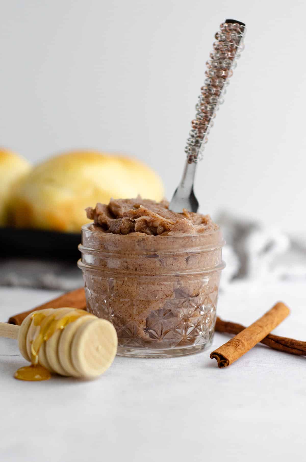 cinnamon honey butter in a small mason jar with a spreader in it, cinnamon sticks around it, and a honey dipper next to it