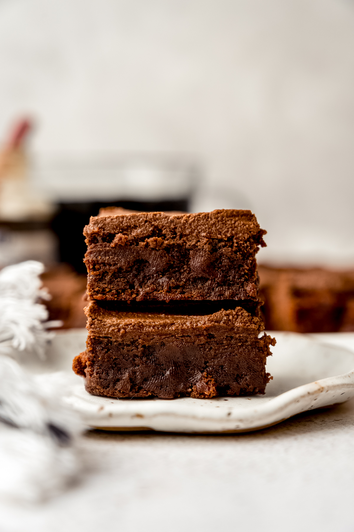 Two coffee brownies stacked on top of each other on a plate with coffee in the background.