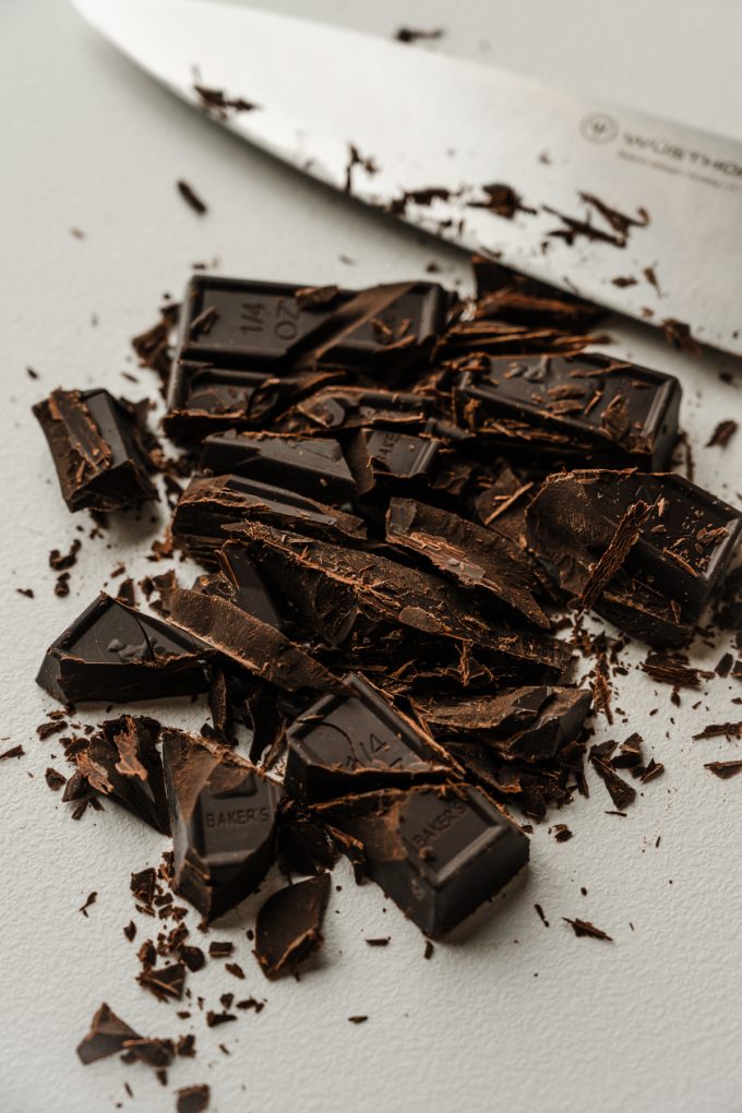 Chopped chocolate on a cutting board with a knife in the background.
