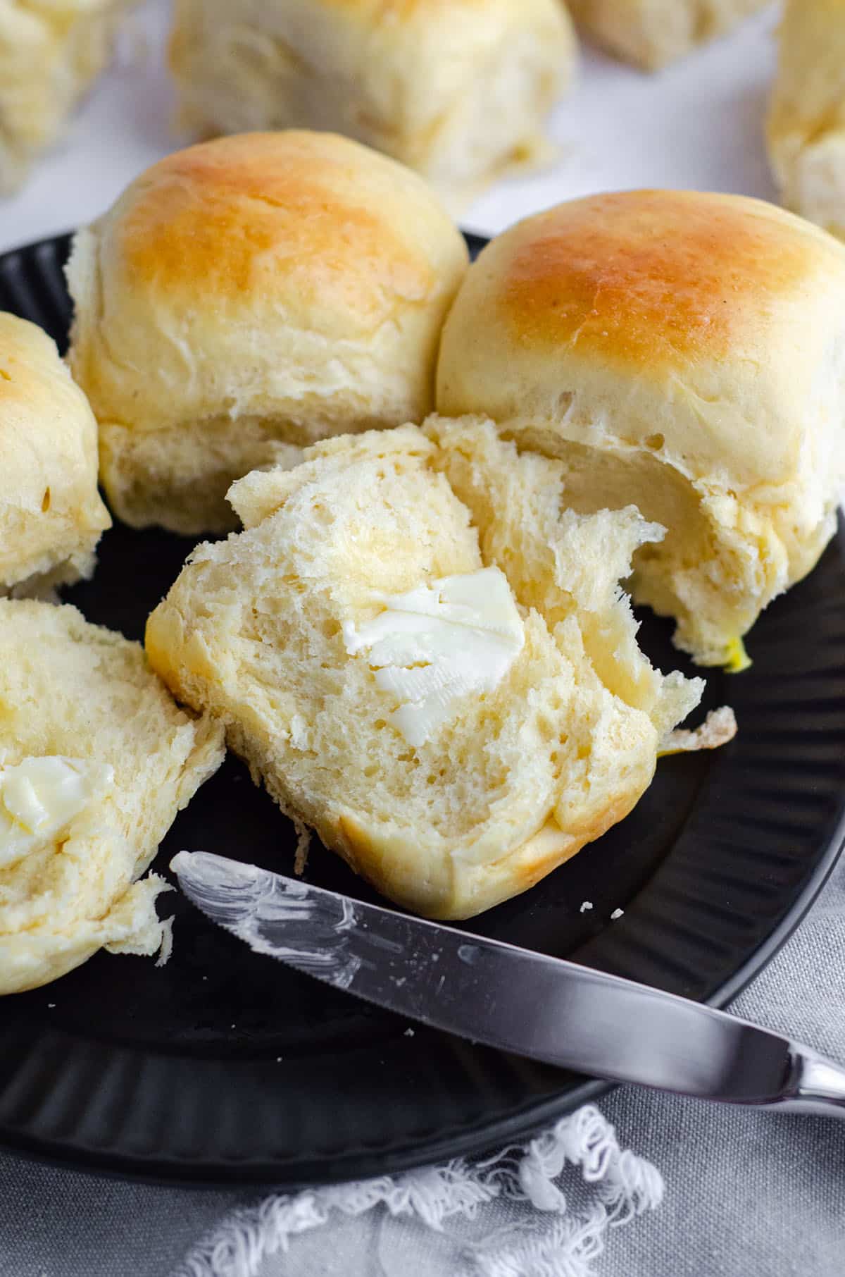 easy yeast rolls on a black plate with a pat of melting butter and a knife