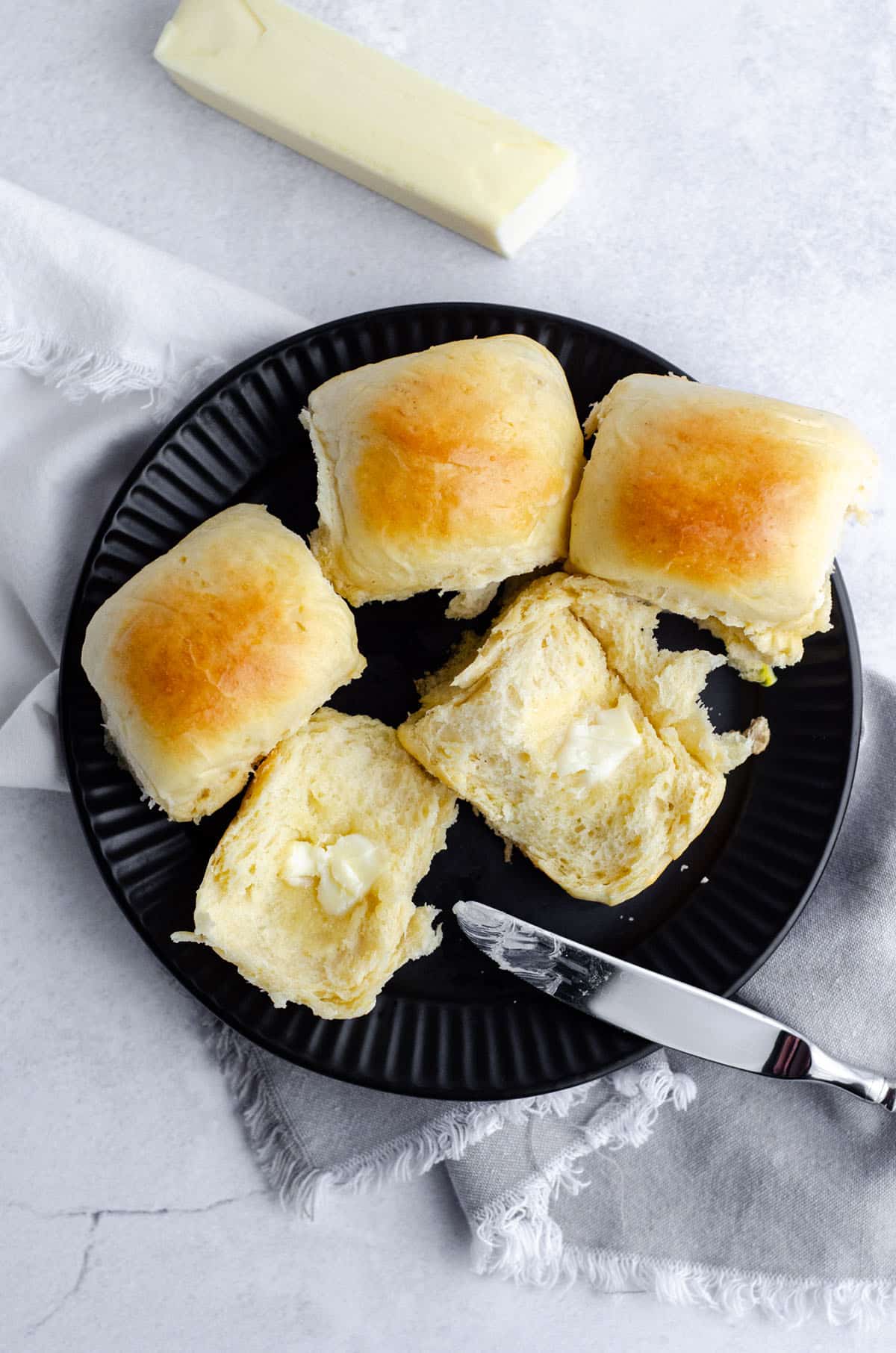 aerial photo of easy yeast rolls on a black plate with a pat of melting butter and a knife