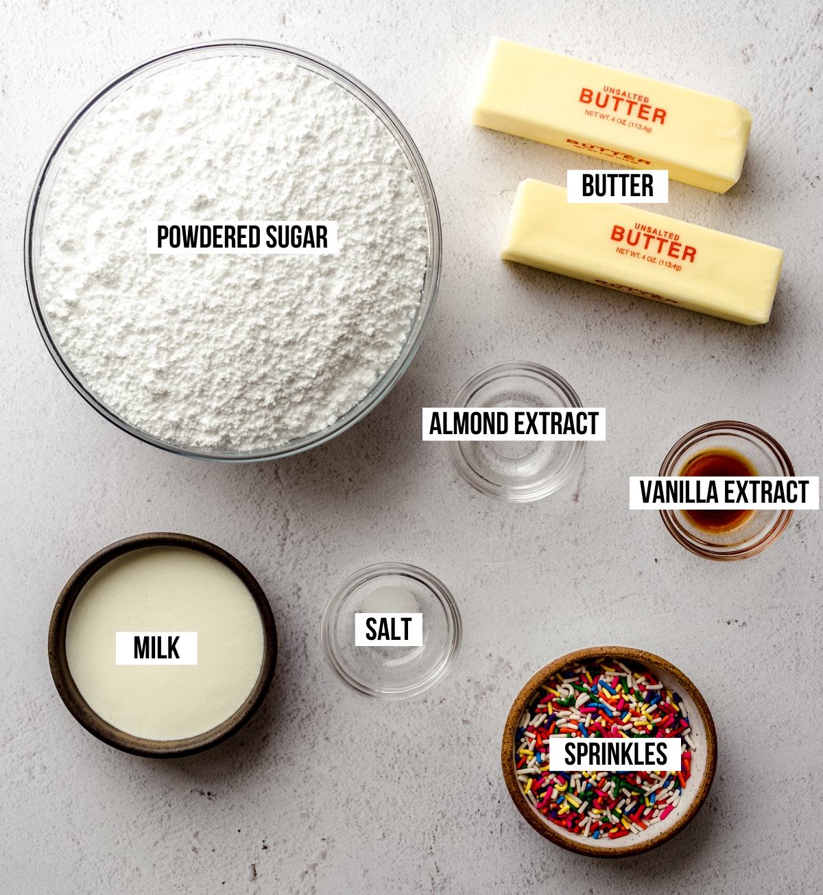 Aerial photo of ingredients for funfetti buttercream on a surface with text overlay labeling each ingredient.