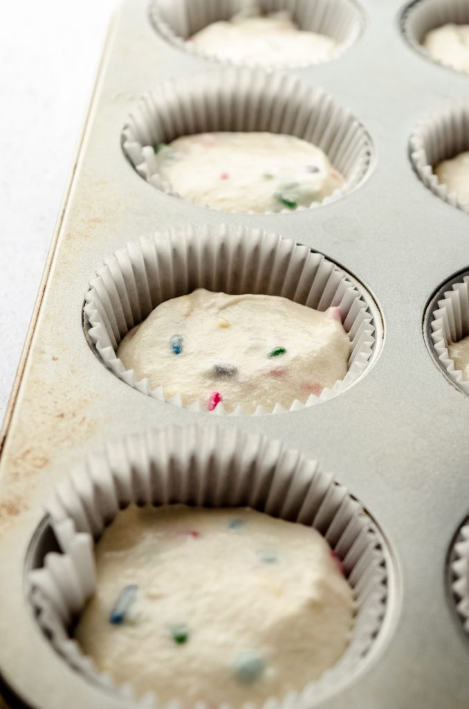Funfetti cupcake batter in the wells of a cupcake pan lined with cupcake liners.
