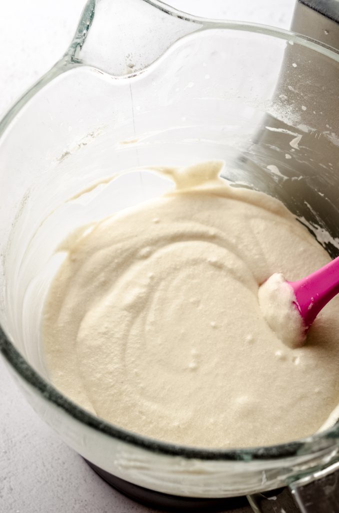 The bowl of a stand mixer with funfetti cupcake batter in it with a bright pink spatula.