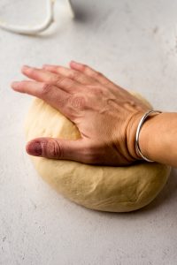 Someone is kneading bread dough with one hand on a surface.